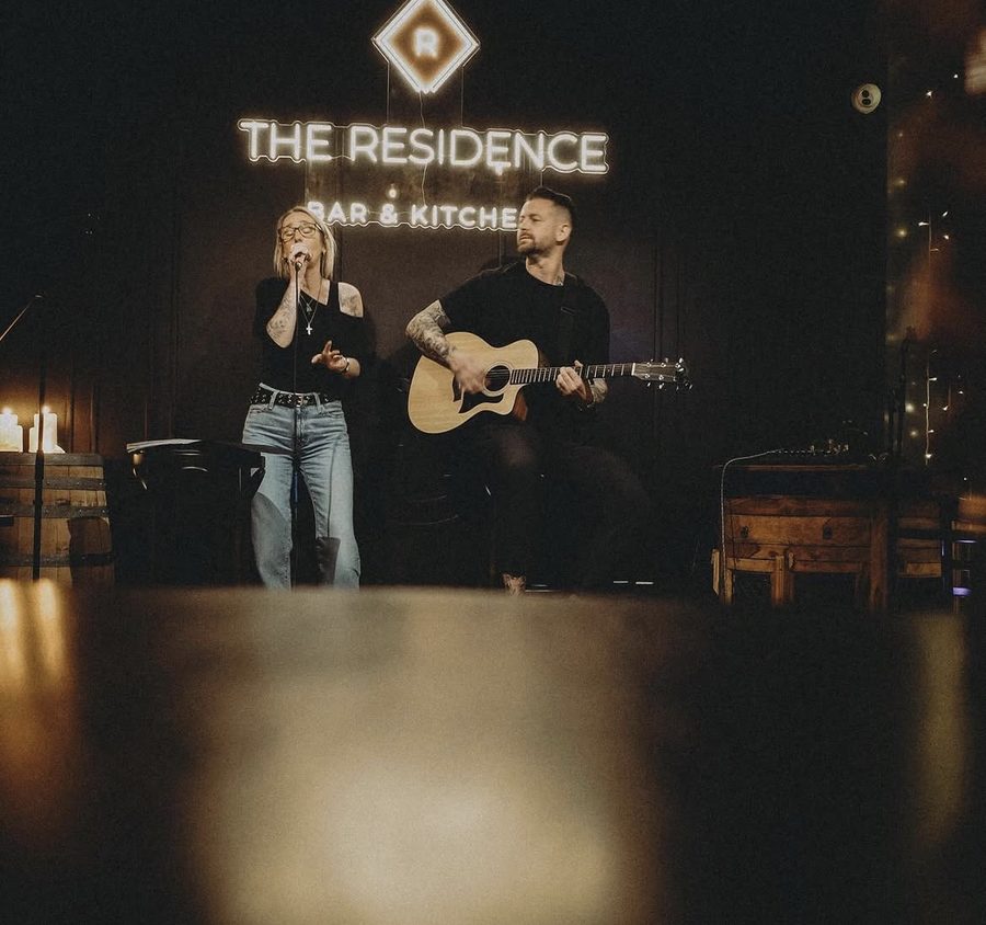 Vix singing and DS on guitar under The Residence neon sign